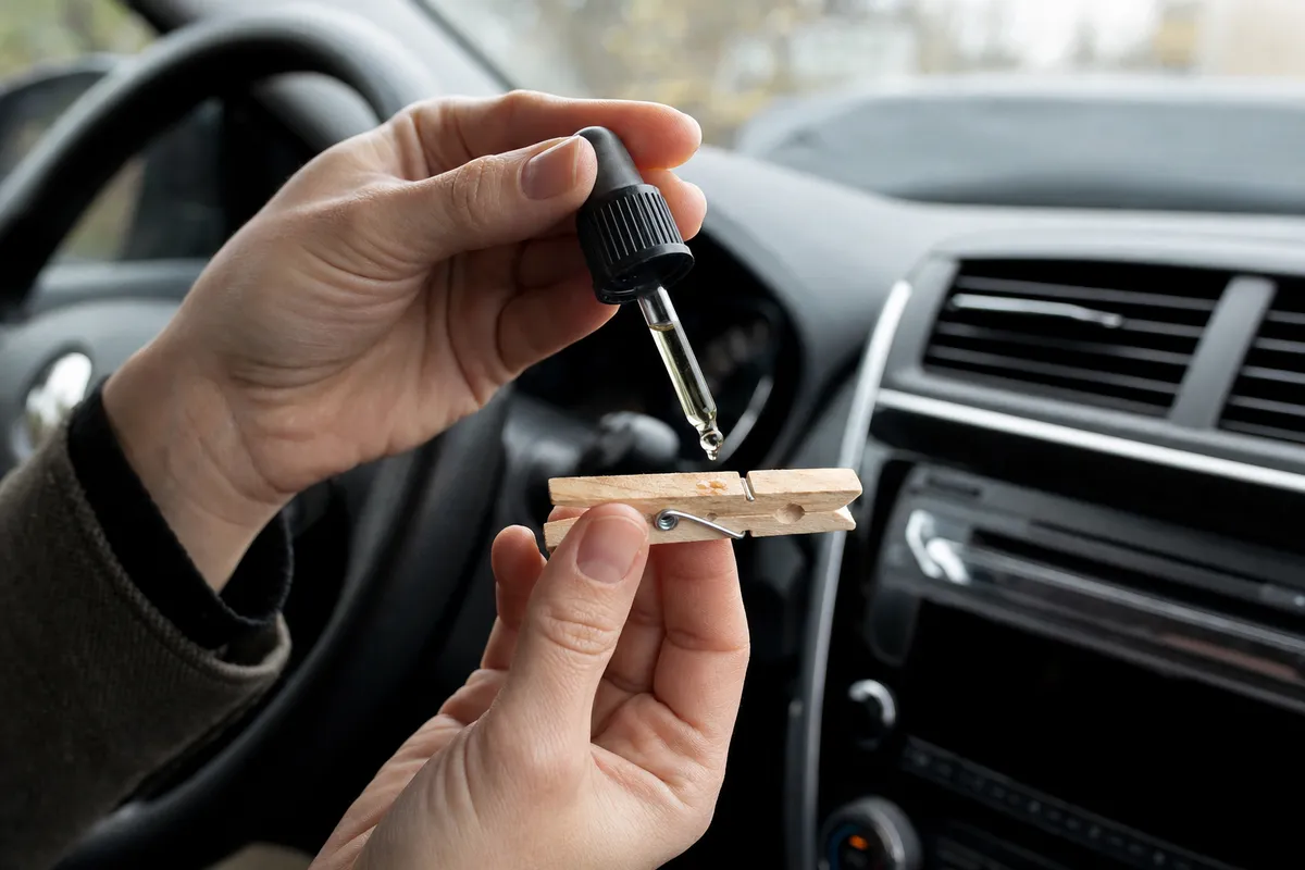 Mani in auto che versano una goccia di olio essenziale su una molletta di legno vicino alla bocchetta dell’aria